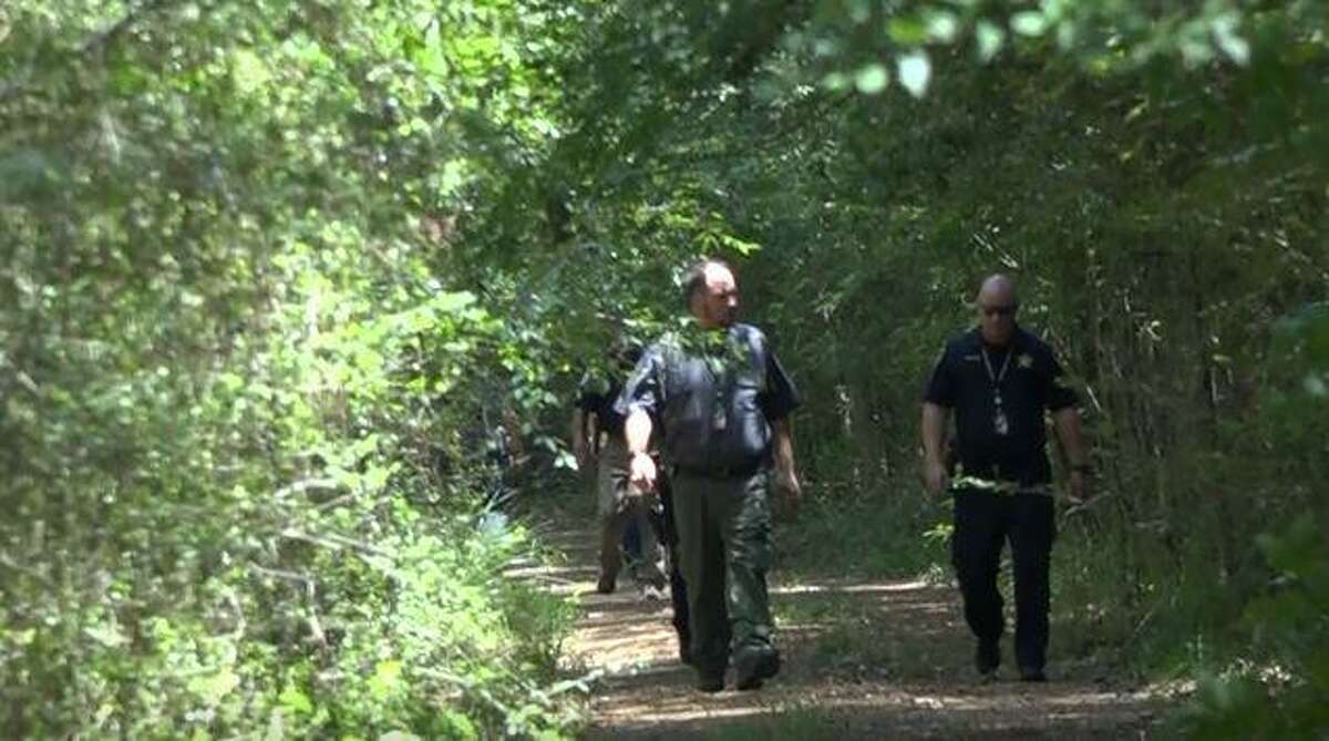 Investigators are seen walking through a wooded area in New Caney where a man and woman were found dead in early June.