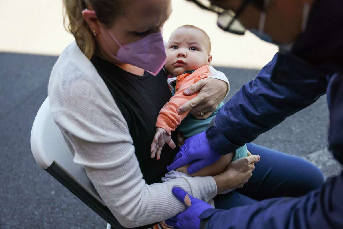 Nurse James Mangalus (right) prepares to give the COVID-19 vaccine Xitlali Campos, 8-months as she is held by mom Loraine Rossi de Campos (left) at UCSF Laurel Heights on Thursday, June 23, 2022 in San Francisco, California.This is the first day that children under 5 are eligible to be vaccinated for COVID-19.