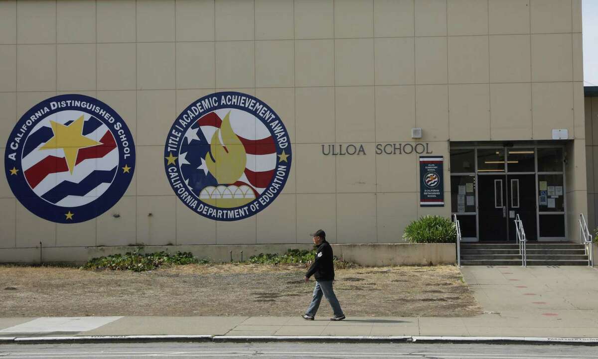 2022年6月28日星期二，加州旧金山，一名行人走过学校大楼上的加州杰出学校和一级学术成就奖标志，旁边是乌略亚小学的标志。