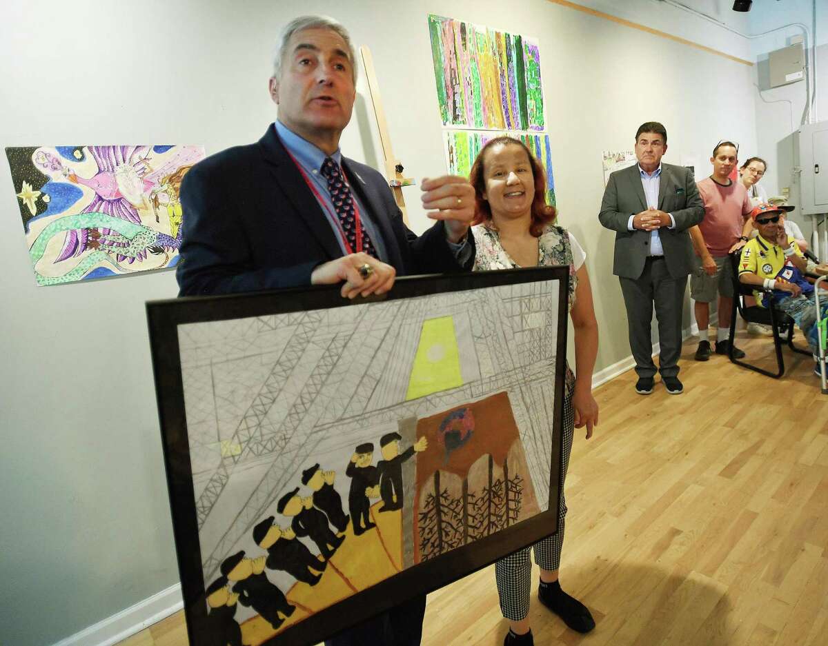 Homes for the Brave CEO Vincent Santilli, left, receives a donated artwork, honoring the victims of the Pearl Harbor attack, from Kennedy Center artist Christina Bevans, right, of Stratford, at the Kennedy Center Daly Arts Co-op in Bridgeport, Conn. on Tuesday, June 28, 2022.