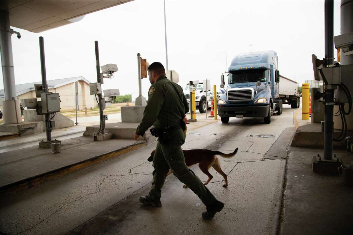 A U.S. Customs and Border Protection agent and a K-9 unit cross a lane as they work at a CBP inspection station on Interstate 35 looking for evidence of smuggling, Wednesday, May 26, 2021, in Laredo.