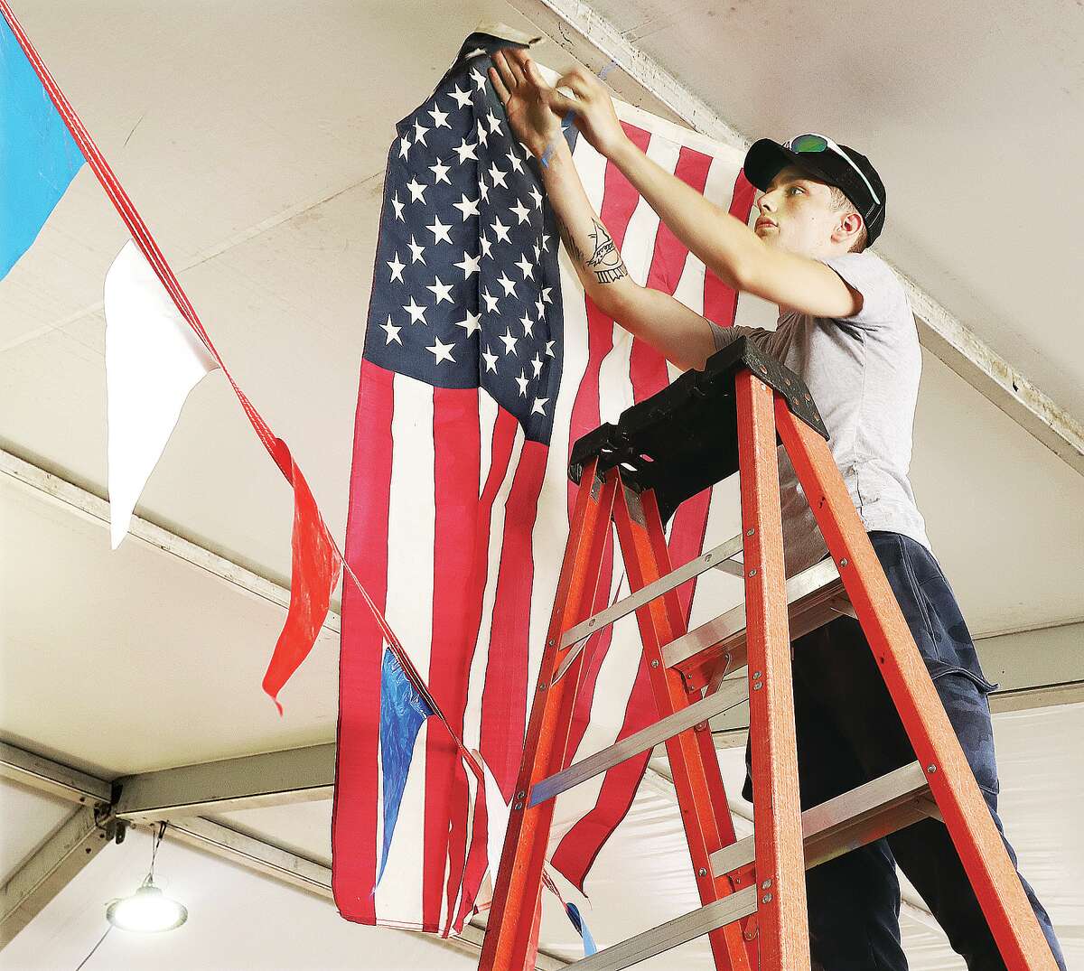 Tristan Acup of Alton hangs flags under the large fireworks tent in West Alton, Missouri, behind the Pit Stop gas station at the intersection of U.S. 67 and Missouri Highway 94. The popular fireworks tent opened last week. Several communities will again this year be firing off public fireworks displays in the area.