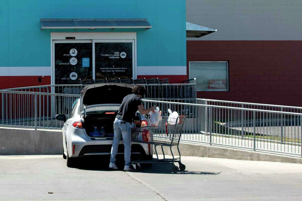 An H-E-B employee loads groceries into a customer’s car at a store.
