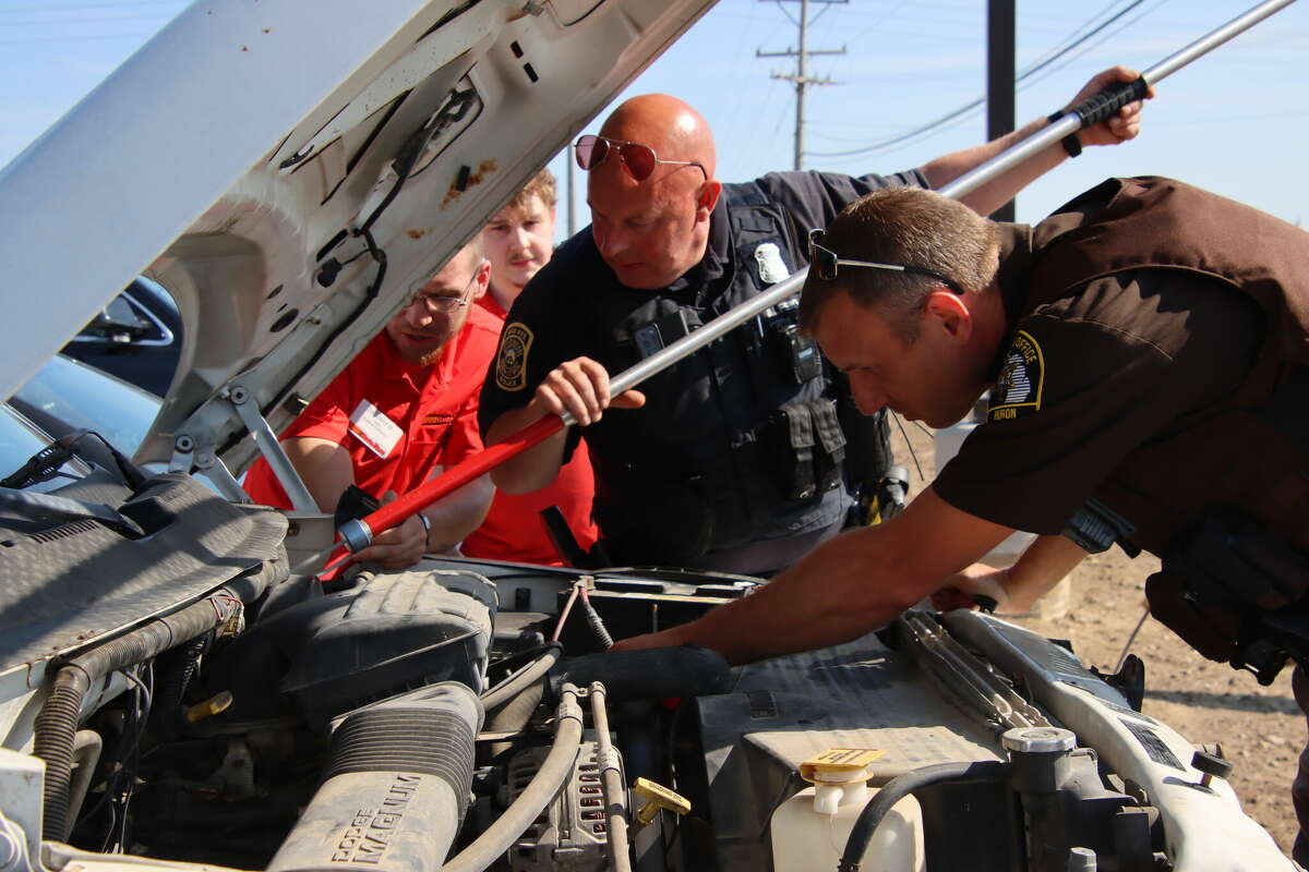 Officer Scott Zalaski of the Bad Axe Police Department, center, and Huron County Sheriff's Dep. Brad Strozeksi, right, work to free a raccoon trapped in the engine compartment of a pickup truck in the parking lot of the new AutoZone store on M-53 in Bad Axe. The truck's driver, Zach Maynard of Sebewaing, far left, and a co-worker helped free the critter from the truck.