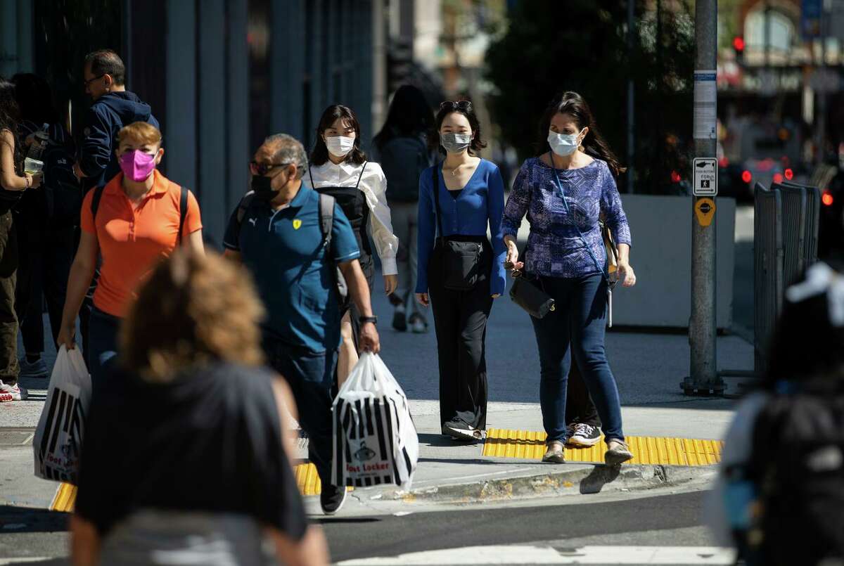 两种新的高传染性和免疫逃避性COVID变体现在在美国占主导地位。周四，戴着口罩的行人走在旧金山。