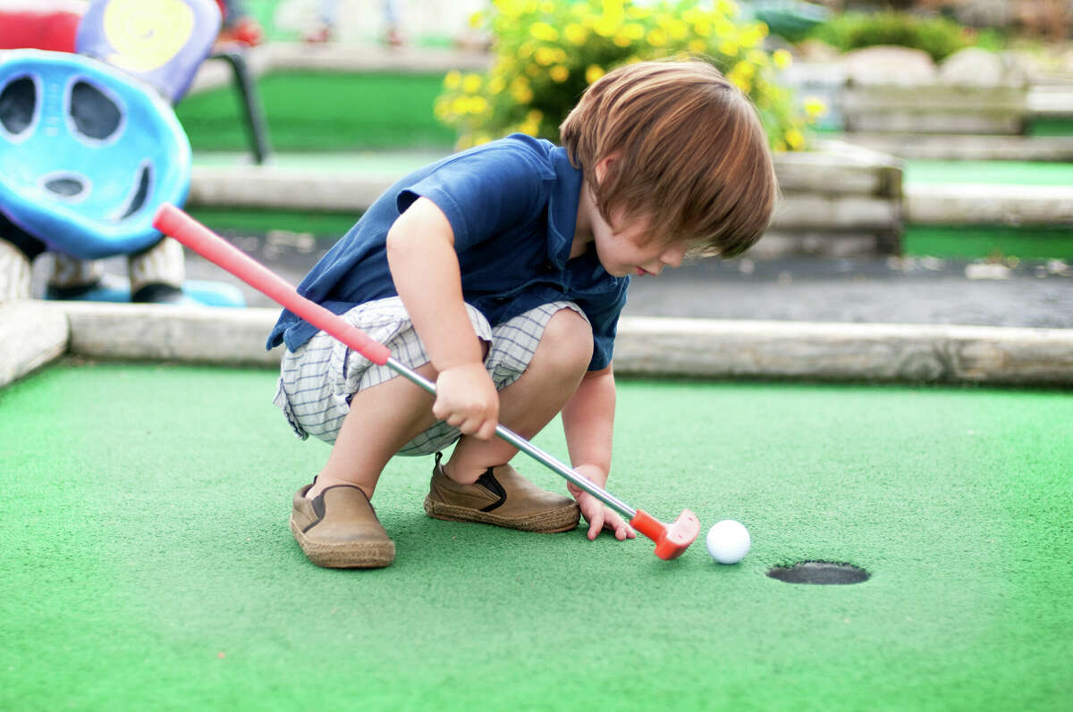 Little boy playing mini golf.
