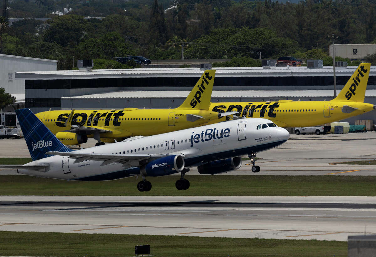 A JetBlue Airlines plane takes off near Spirit Airlines planes at the Fort Lauderdale-Hollywood International Airport in May 2022.