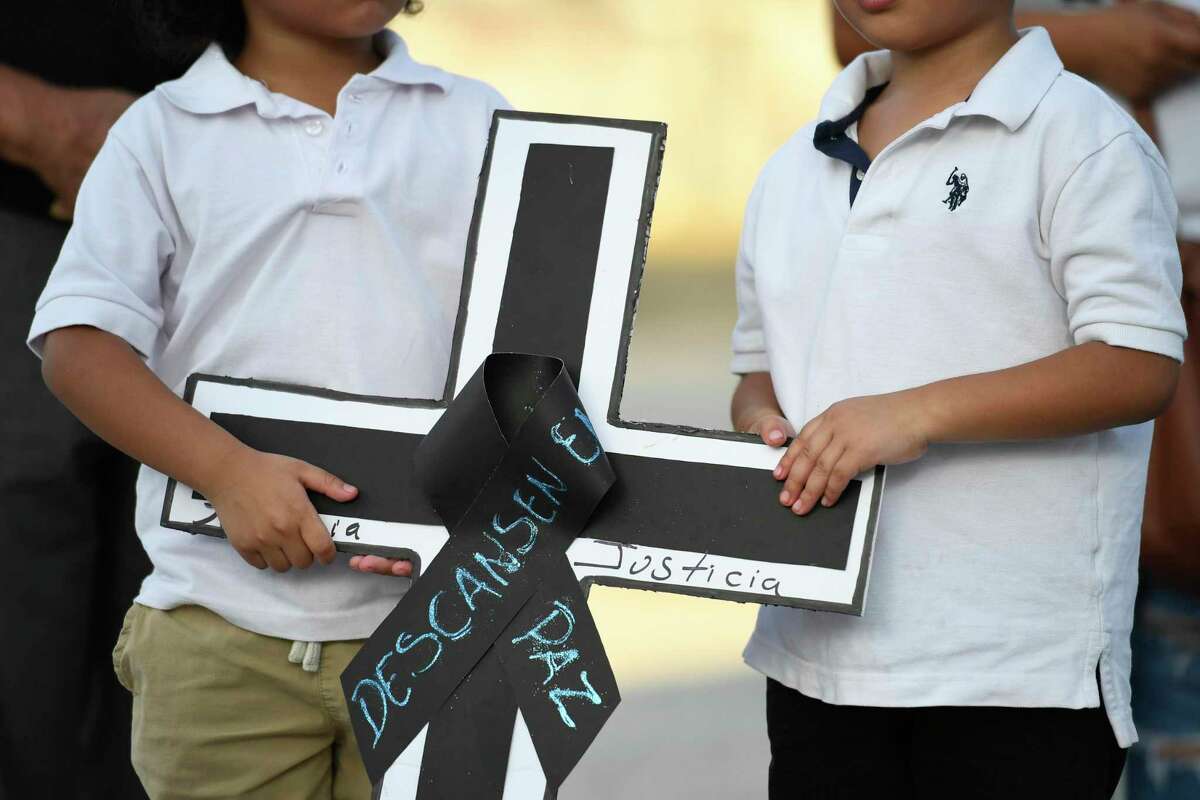 Two boys hold a cross during a vigil held for the migrants that died in a semi-trailer in San Antonio at the FIEL headquarters Tuesday, June 28, 2022, in Houston.