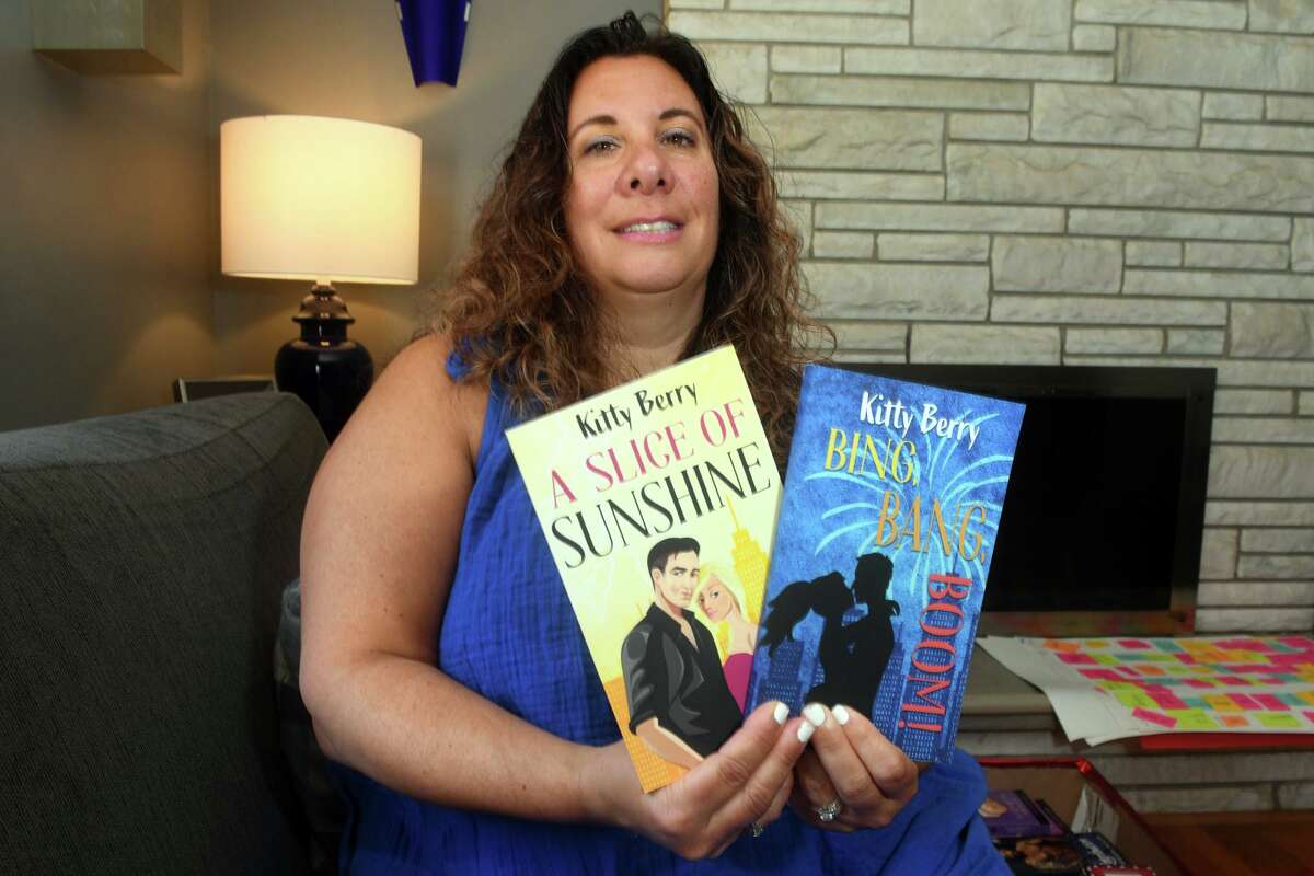 Author and RomantiConn organizer Rachel Cappello, aka Kitty Berry, poses with a couple of her romance novels in her home in Trumbull, Conn. July 1, 2022.
