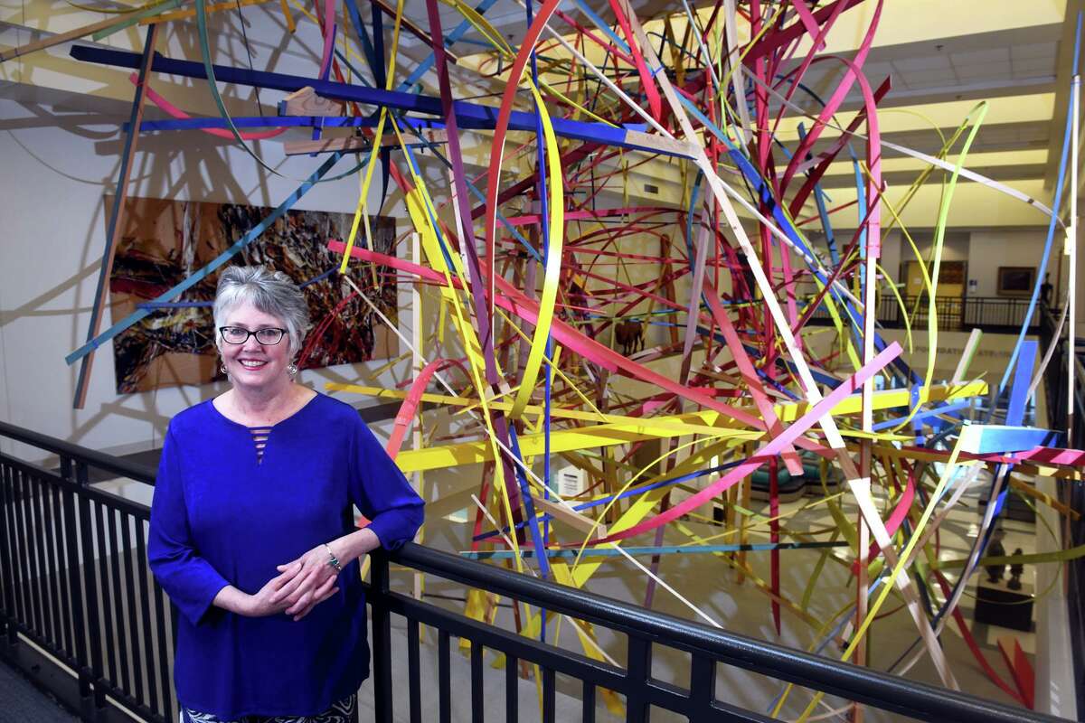 Robbin Zella, Director of the Housatonic Museum of Art, poses in front of a sculpture by artist Jongil Ma installed above the main atrium of Housatonic Community College, in Bridgeport, Conn. June 29, 2022. The sculpture, titled “Be There When You Return” was commissioned by Zella and installed in 2021. Zella, who has curated Housatonic’s vast art collection since 1998, has announced her retirement.