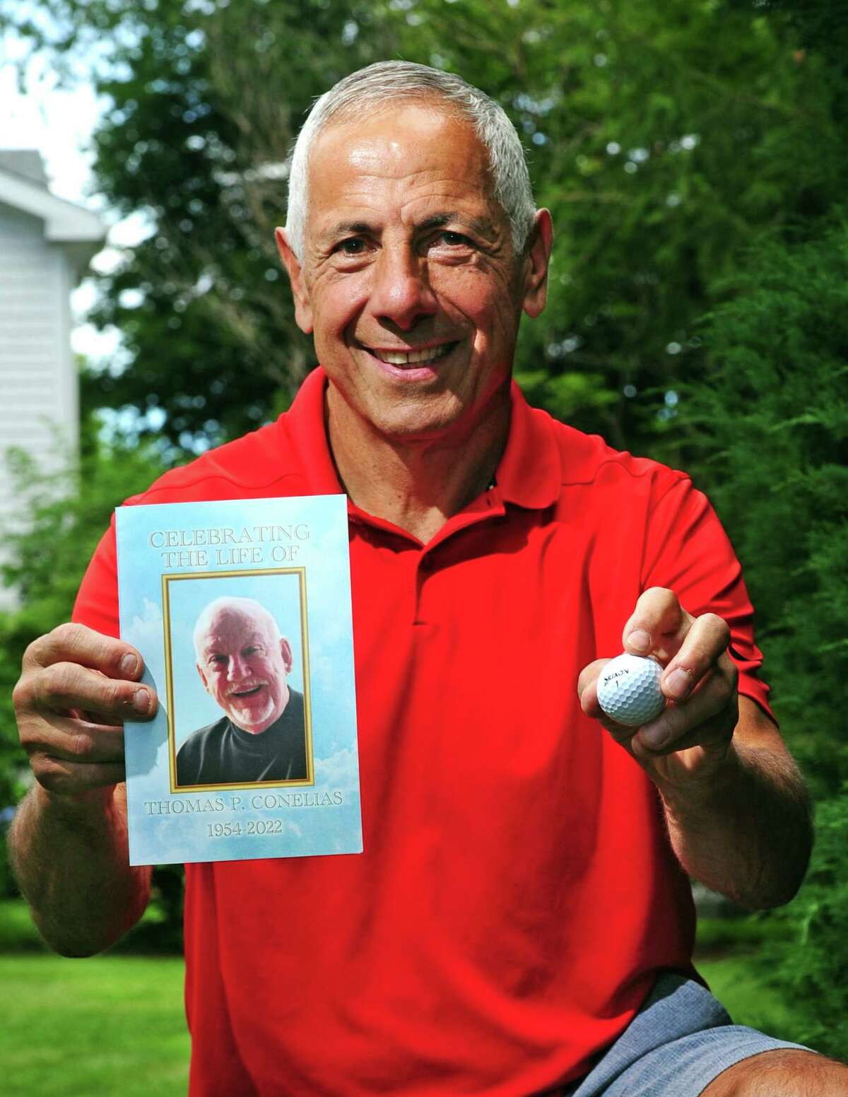 Peter Carino, who recently scored a hole in one at the town's municipal golf course, poses at his home in Greenwich, Conn., on Tuesday June 28, 2022. He did it on May 20 which was also the day his best friend Tom Conelias, (pictured on card) who died suddenly in late April, had done in 2009. They even did it on the same hole, the seventh. The day is also significant because May 20 was the day before Conelias' father's funeral and the birthday of Conelias' late son who had been killed in a car accident when he was 10 years old. Carino felt this was a sign and will try to have the golf ball buried with his friend when the headstone is put in place.