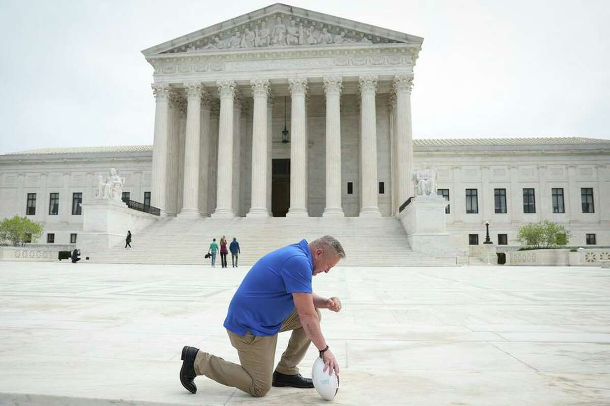Joe Kennedy, a former assistant football coach at Bremerton (Wash.) High, takes a knee in front of the Supreme Court in Washington, D.C., after his legal case was argued before the justices in April. He won the prayer case.