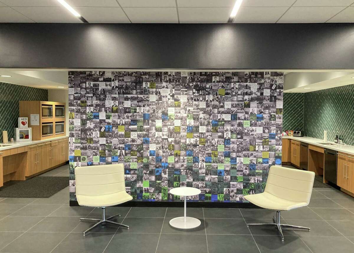 A wall with a grid of employee photos with inspirational notes such as “Help each other succeed at work and in life” provides a backdrop to the seating area outside the kitchen on the 12th floor.