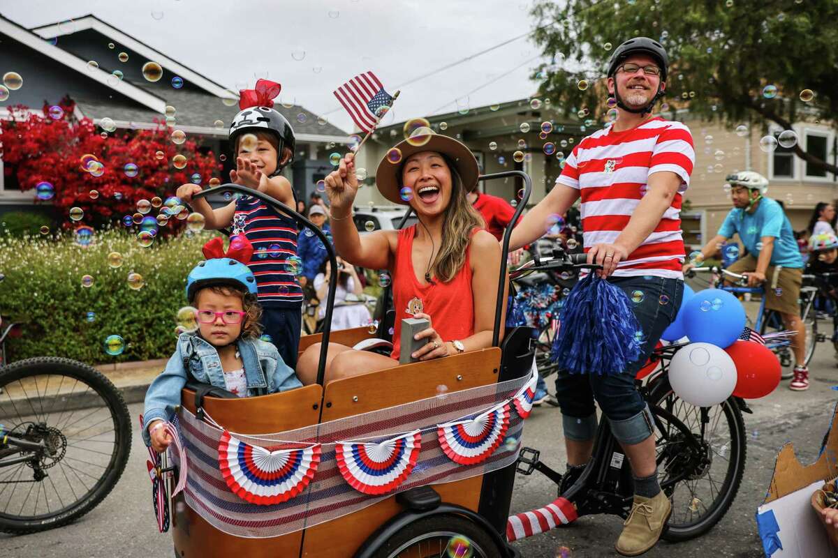 Evie Grubb Tang, 3 (left); Austin Grubb Tang, 5; mom Fiona Tang; and dad Ted Grubb greet a friend as they bike in the parade in the town of Alameda, which draws crowds from around the region.