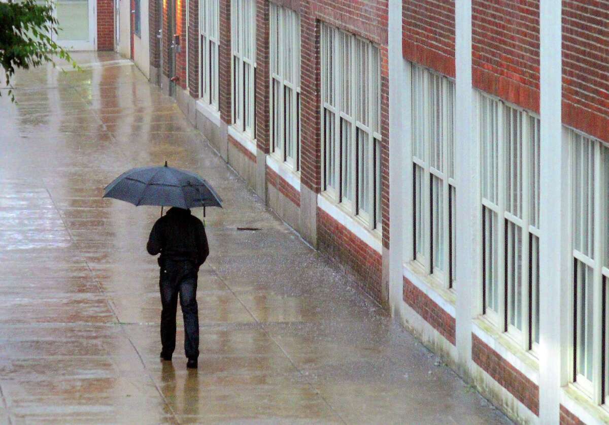 In this file photo, a pedestrian walks along the side of Reads Art Space apartments during a thunderstorm in downtown Bridgeport, Conn. Showers are expected to impact Connecticut later Tuesday, July 5, 2022, with thunderstorms expected overnight.