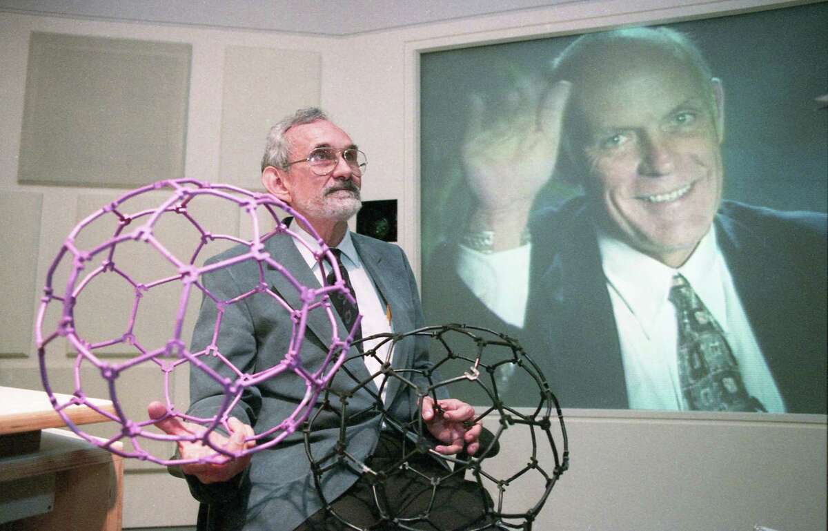 10/09/1996 - Rice University chemistry Professor Robert Curl, left, holds models of a new carbon molecule he discovered along with fellow Rice Professor Richard E. Smalley, shown in the background on a video screen, at Rice University in Houston. The pair along with Harry Kroto of the University of Sussex in Brighton, England, were awarded the Nobel Prize in Chemistry, Wednesday, for their 1985 discovery of a family of soccer ball-shaped carbon molecules known unofficially as "buckyballs.''