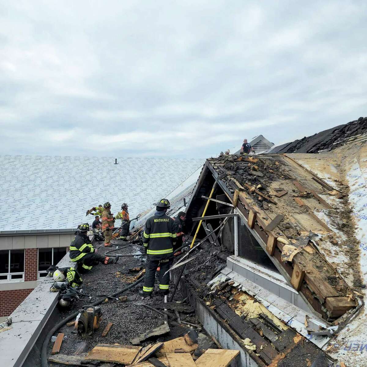 Firefighters inspect the damaged roof at New Milford High School after Tuesday’s fire.