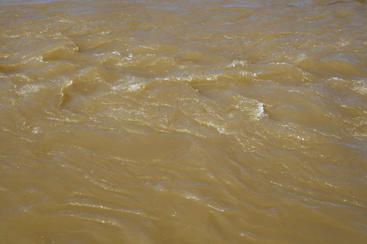 Turbid stream of water. Spring river with brown muddy water. Close-up.