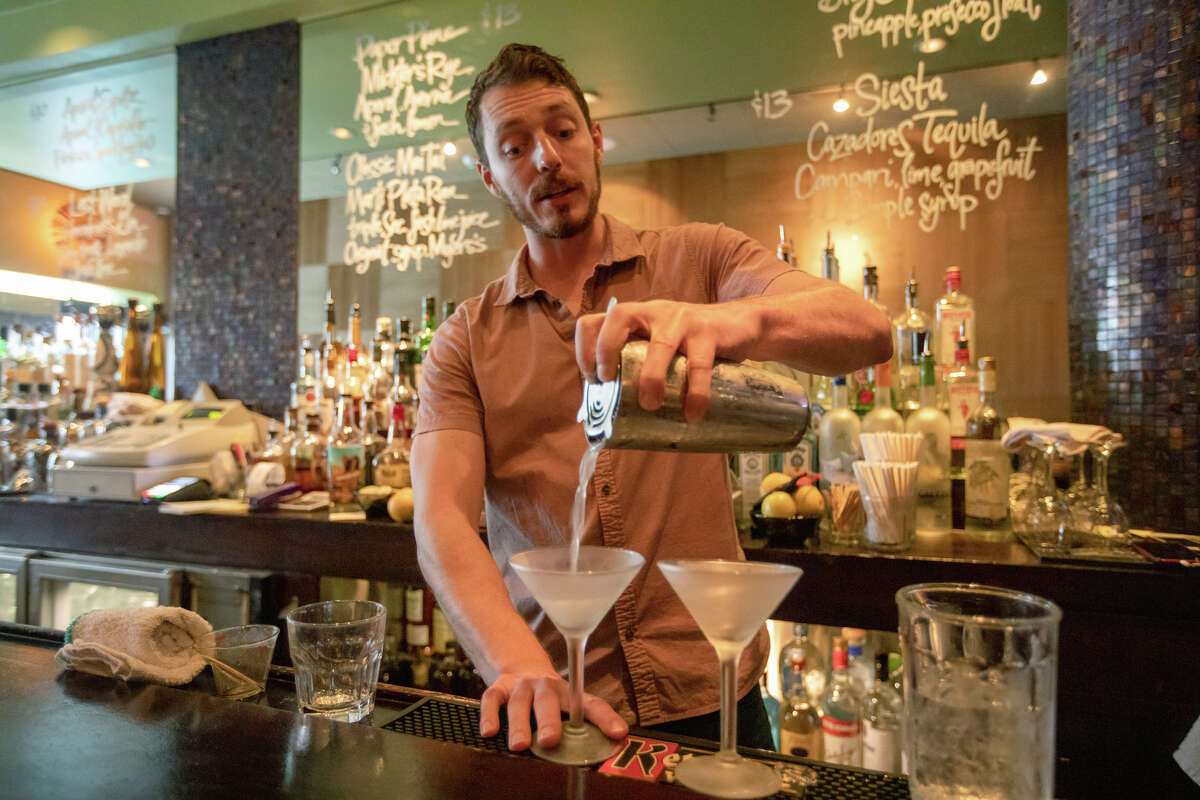 Bartender Ian Whittaker prepares cocktails behind the bar counter at Tony Niks in San Francisco, California on July 7, 2022. Scala, a longtime patron and manager, is the new owner of Tony Niks, an old-fashioned bar in the heart of North Beach. He is committed to preserving his legacy.