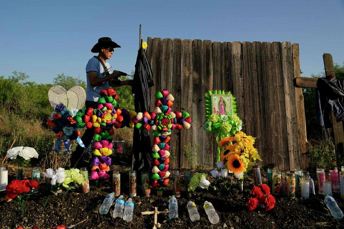 A man secures a cross to a makeshift memorial where dozens of migrants were found dead in San Antonio. A new report says those victims were coerced into a smuggling that turned deadly.