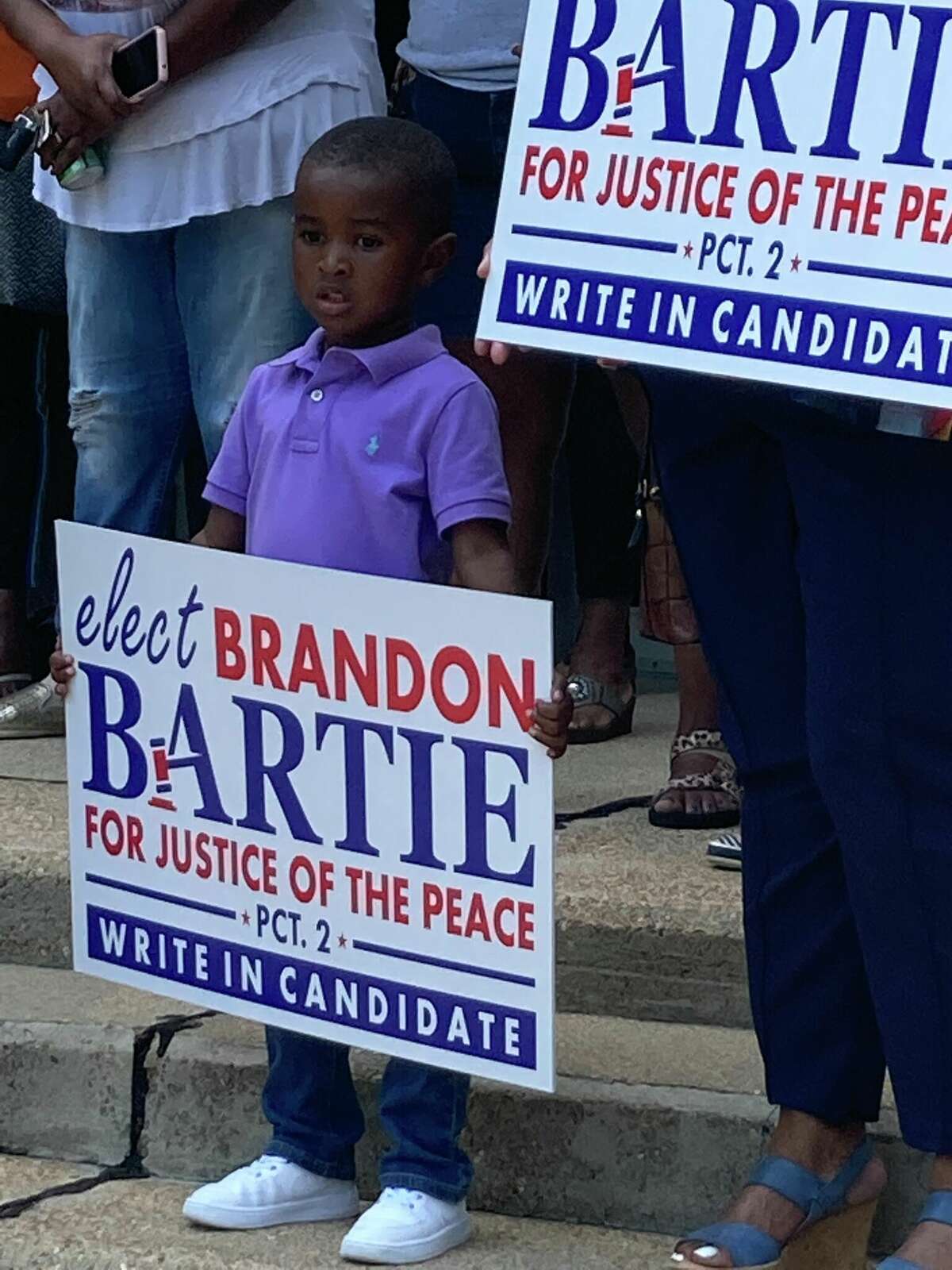 Brendan Bartie, son of candidate Brandon Bartie, holds signs for his father's campaign at press conference.