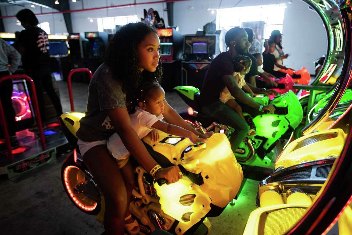 Maddison Graham, 16, and Aliyah Peters, 2, play together an interactive motorcycling video game at Cidercade in EaDo.