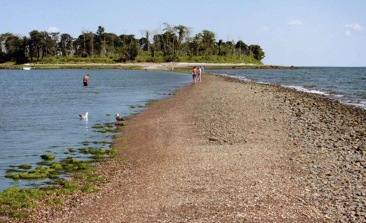 People traverse the tombolo, or sandbar, that leads to Charles Island at Silver Sands State Park in Milford, Conn. A music festival planned on a floating stage in the waters off the island has been postponed this summer, after issues with the event’s insurance, its organizers said.