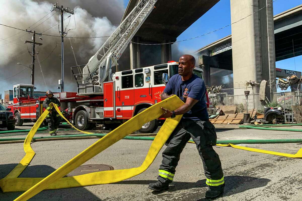 2022年7月11日星期一，加州西奥克兰580高速公路下发生火灾，奥克兰消防部门消防员凯文·摩尔在现场准备水管。