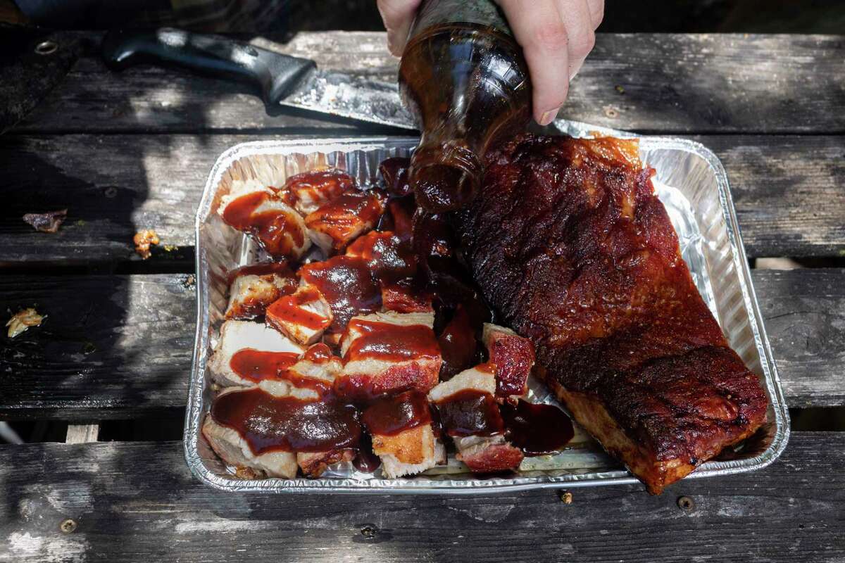 Chuck Blount pours barbecue sauce over pieces of hickory wood-smoked pork belly to turn them into burnt ends.