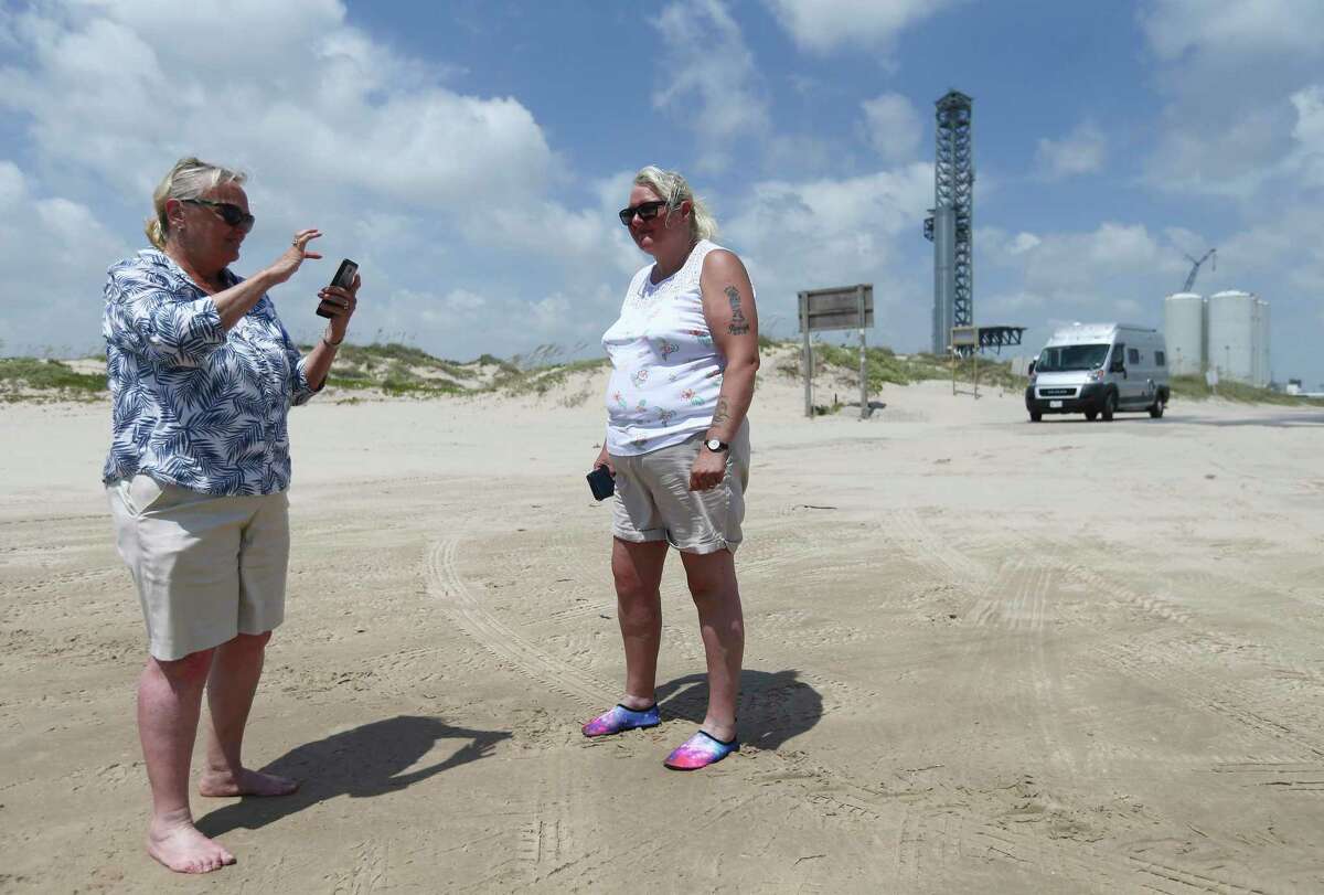 Jeanne Nelson (from left) and Veronica Gray of Scotland snap pictures on Boca Chica Beach near Starbase on July 1. In the background, SpaceX Booster 7 is seen on the launch pad. During static testing Monday, the booster burst into flames, possibly slowing plans for a SpaceX orbital launch from South Texas.