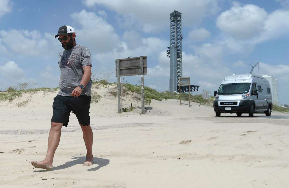William Stark of Dallas walks on Boca Chica at the start of the July 4 holiday weekend. In the background, SpaceX Booster 7 is seen on the launch pad. During static testing Monday, the booster burst into flames, possibly slowing plans for a SpaceX orbital launch from South Texas.