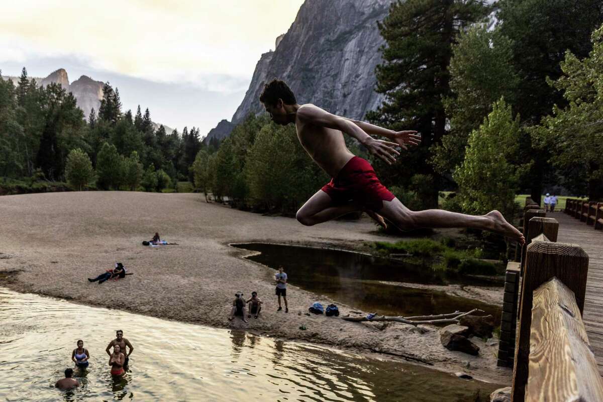 Mizobek Juraev leaps from Swinging Bridge into the Merced River below as a tinge of smoke from the Washburn Fire can be seen in Yosemite National Park, Calif. Tuesday, July 12, 2022.