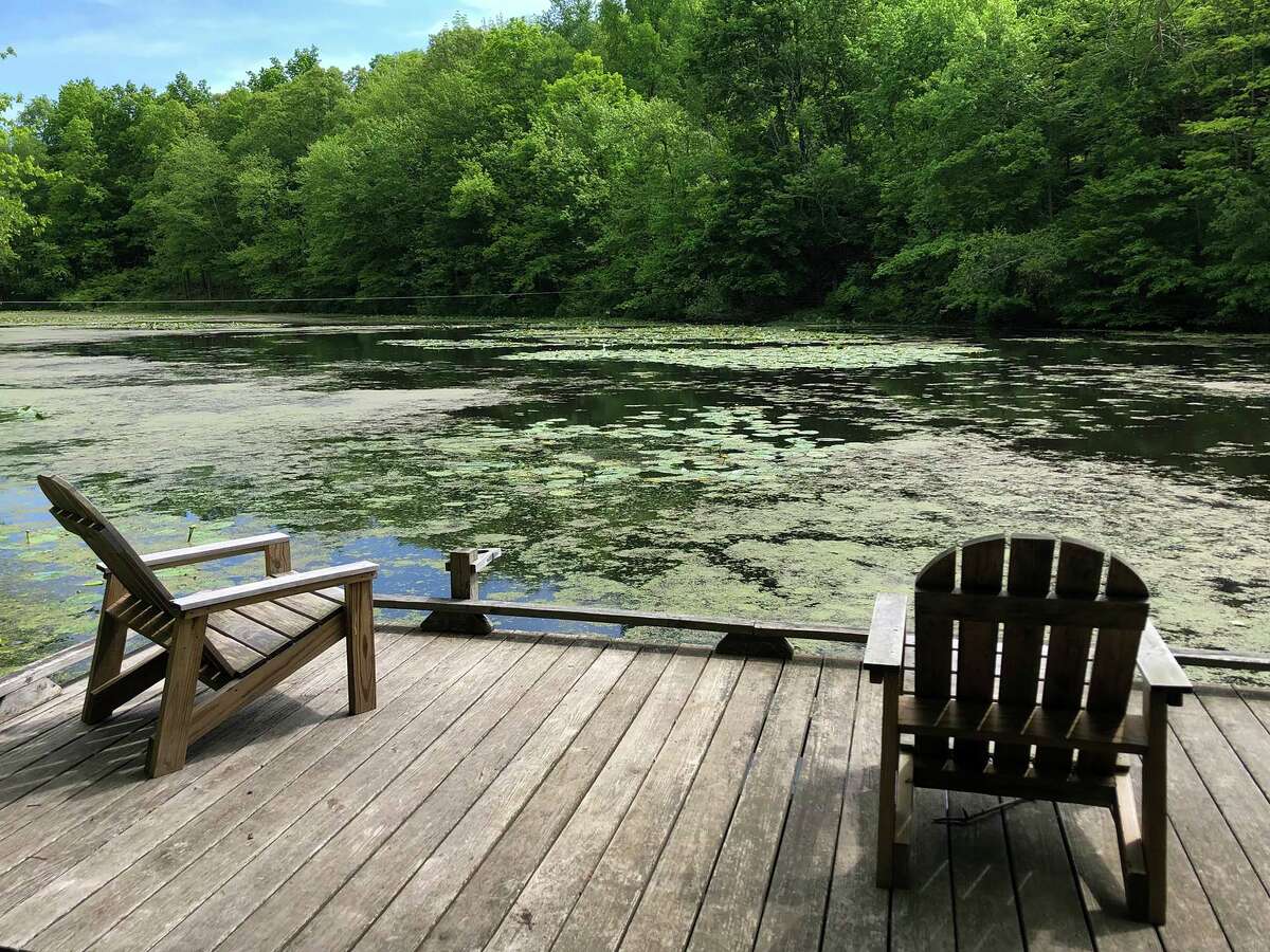 A pair of Adirondack chairs sit on a dock overlooking the pond.
