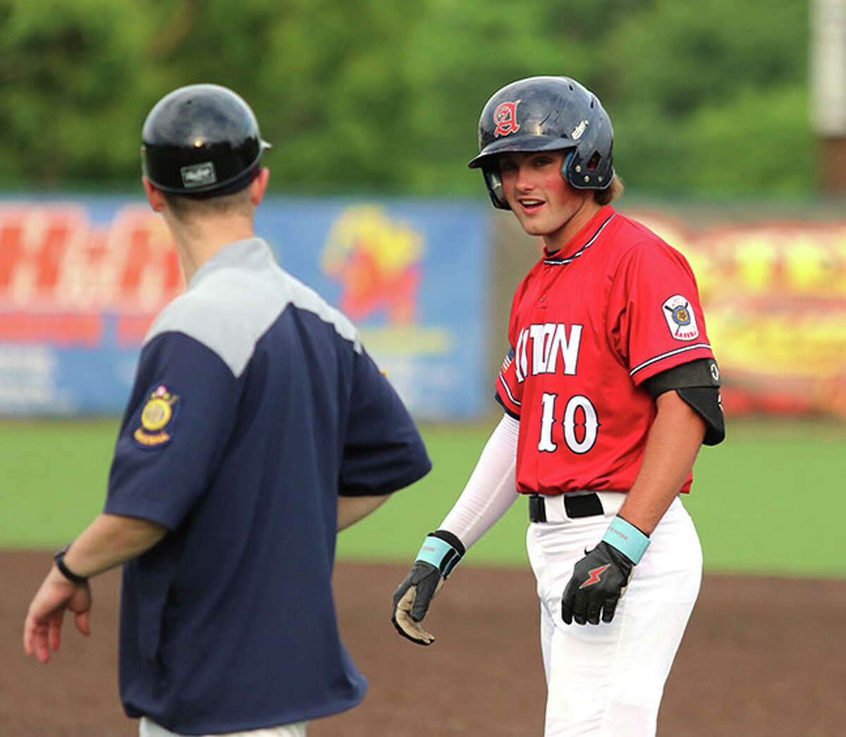 Alton's Hayden Sherman (right) talks with first base coach Chris Ford after reaching base in a game earlier this season in Alton. Post 126 was back at Hopkins Field on Tuesday night and shut out Troy Father McGivney 4-0.