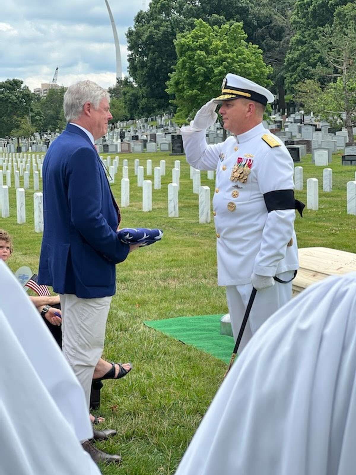 An offier presents a flag to Sam Baker and salutes his father, Rear Admiral Edward Baker, Jr. during services on July 8 in  Arlington National Cemetery.