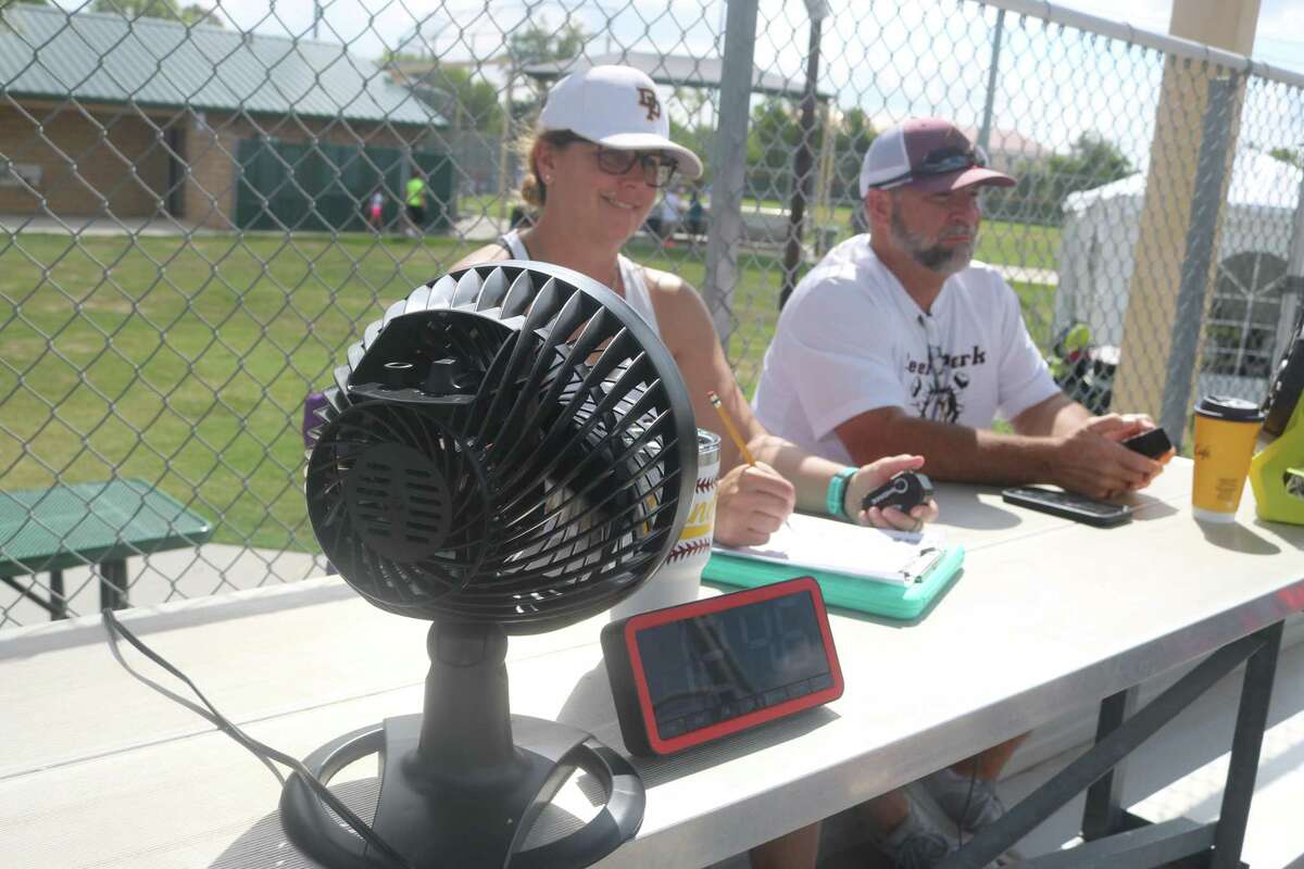 With the help of a fan to ward off the heat, Steve and Alicia Randall, the parents of Deer Park 11s all-star Nolan Randall, do their part to make the South Zone Tournament run smoothly Thursday. They kept track of pitches and ran the scoreboard.