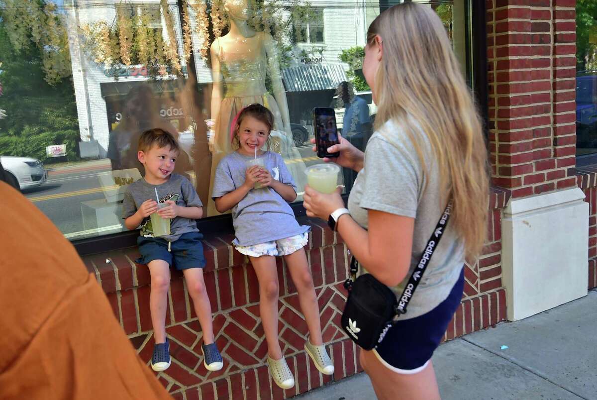 Eduarda Theodoro snaps pictures of her kids Mason, 3, Harper, 7, with their drinks from Lemon Nate's drink stand during the Darien Chamber of Commerce’s Darien Sidewalk Sales event for businesses up and down Post Road in Darien, Conn., on Friday July 15, 2022. The sidewalk sales will also run from July 16, 10 a.m. to 5 p.m.