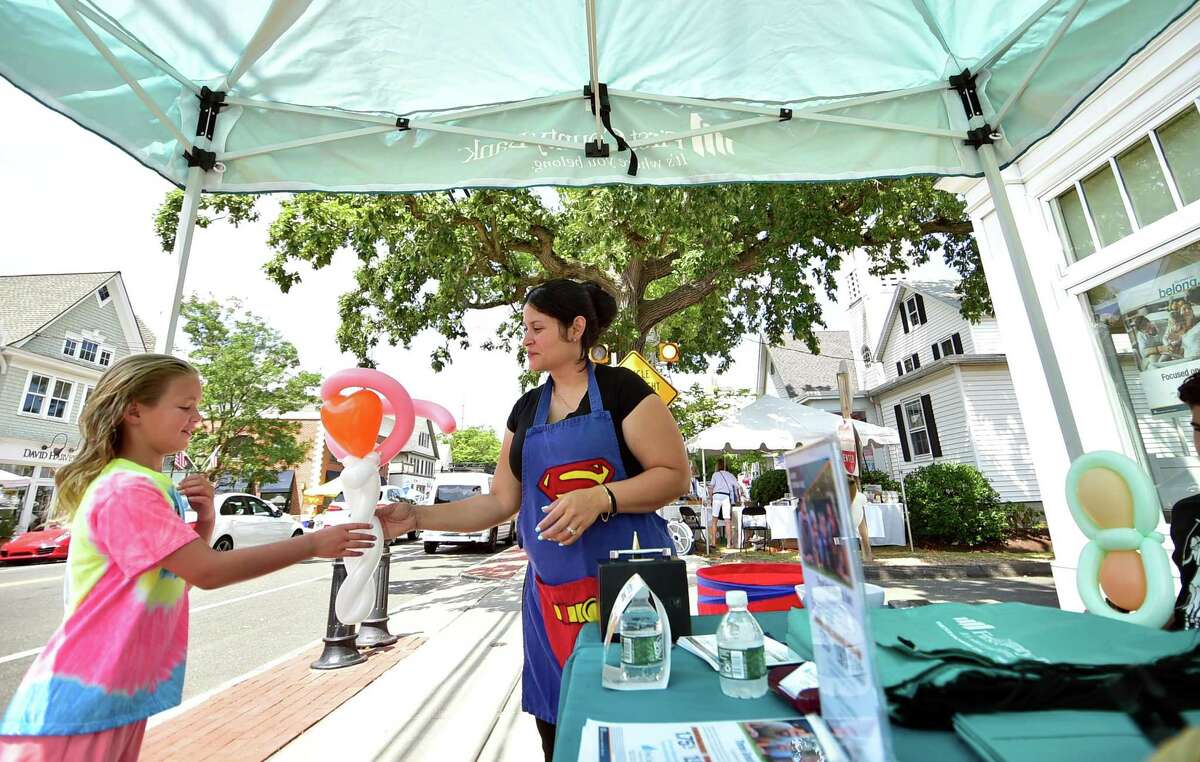 Kathleen Steidel gives a balloon to Anne Illingworth, 8, at the First County Bank tent during the Darien Chamber of Commerce’s Darien Sidewalk Sales event for businesses up and down Post Road in Darien, Conn., on Friday July 15, 2022. The sidewalk sales will also run from July 16, 10 a.m. to 5 p.m.