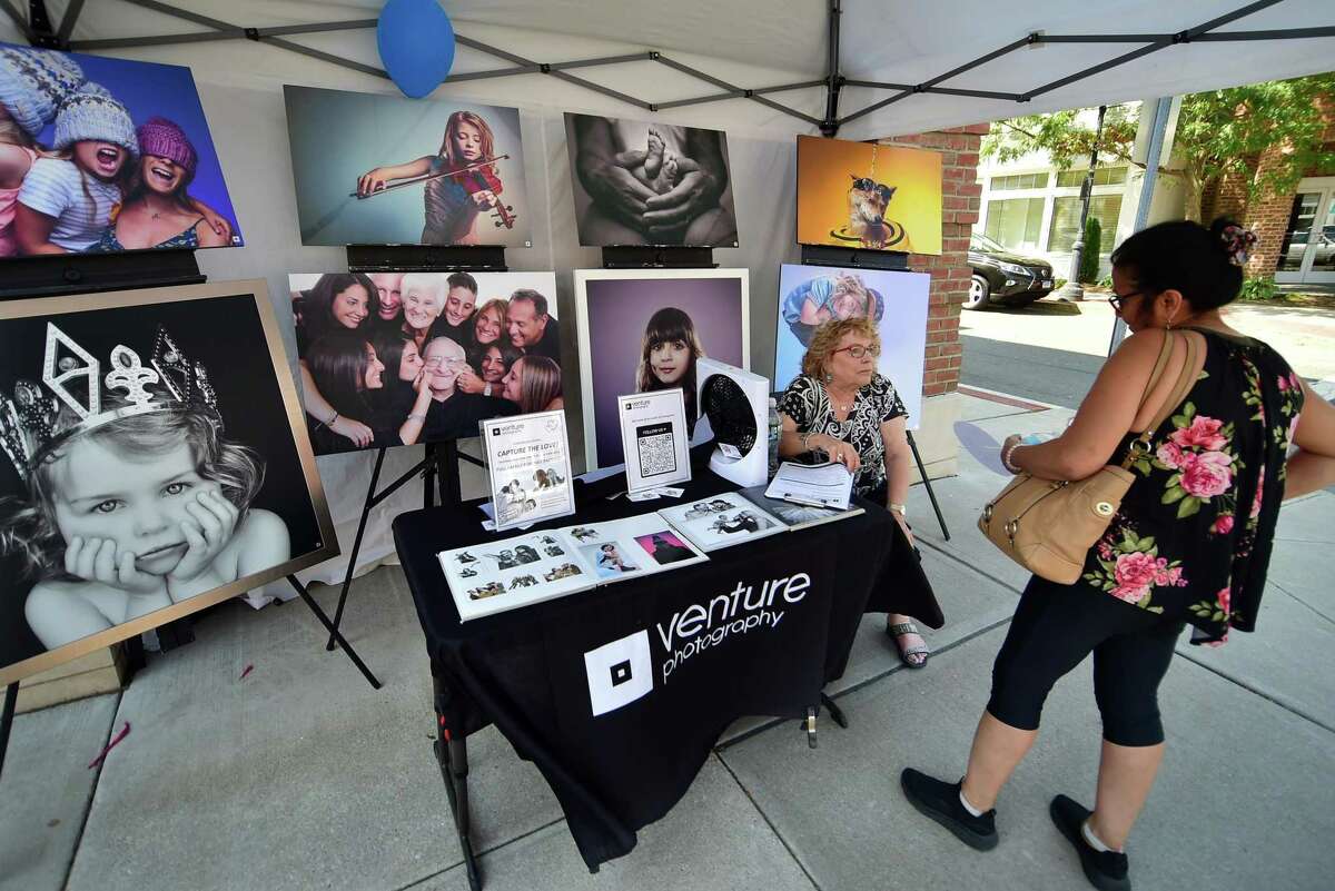 Venture Photography representative Barbara Sage gets Susy Touma, right, interested in entering a drawing for a free portrait session during the Darien Chamber of Commerce’s Darien Sidewalk Sales event for businesses up and down Post Road in Darien, Conn., on Friday July 15, 2022. The sidewalk sales will also run from July 16, 10 a.m. to 5 p.m.