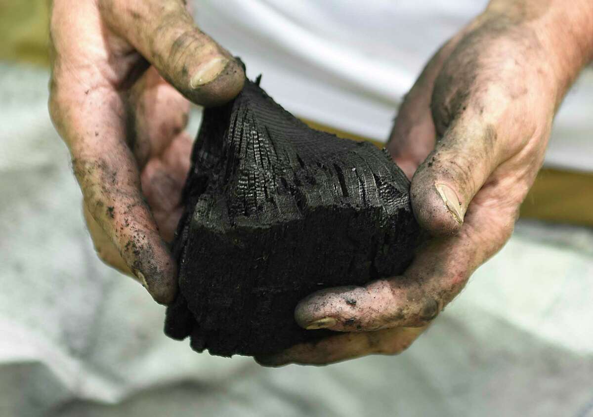 Versailles Farms owner Steve McMenamin shows a chunk of biochar, a form of charcoal used to improve soil functions, at Versailles Farms in Greenwich, Conn. Wednesday, July 13, 2022. Apart from growing dozens of varieties of produce, the farm has an operation that produces high-quality organic charcoal from old-growth oak trees. Versailles Farms sells lump charcoal, activated charcoal, hookah charcoal, and biochar.