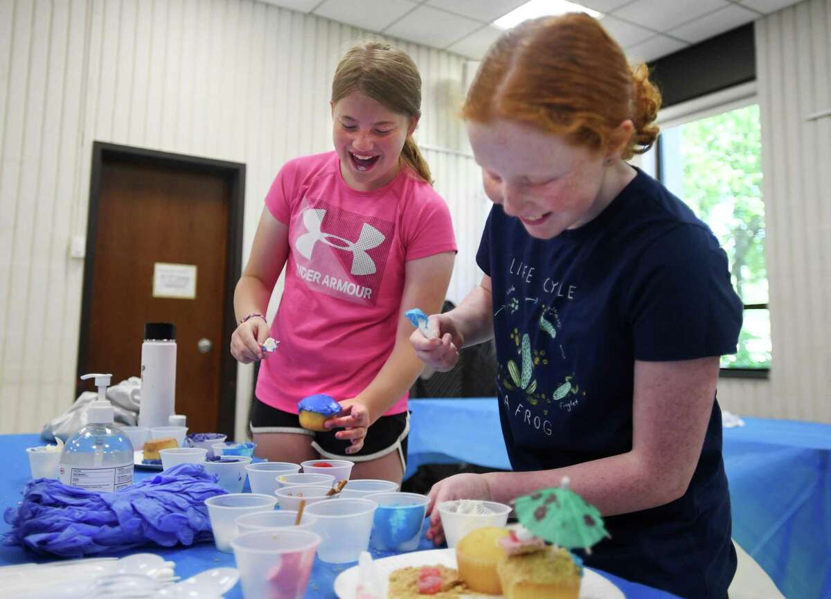 Friends Charlotte Ruddock, 11, left, and Reese Hogan, 9, both of Trumbull, share a laugh as they decorate cupcakes during the Trumbull Health Department's Cupcake Wars event for children at the Trumbull Library in Trumbull, Conn. on Tuesday, July 19, 2022.