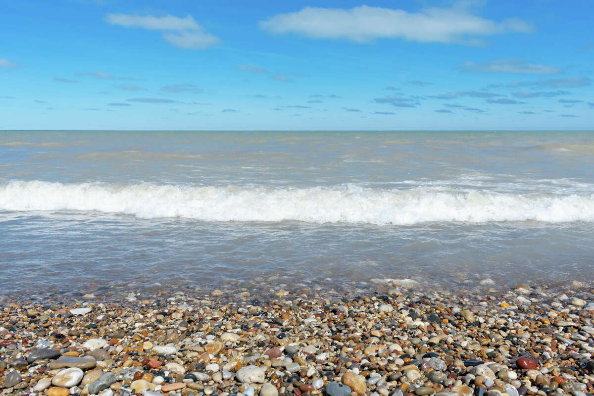 Waves rolling in over rocky shoreline of Lake Michigan on a clear blue day.