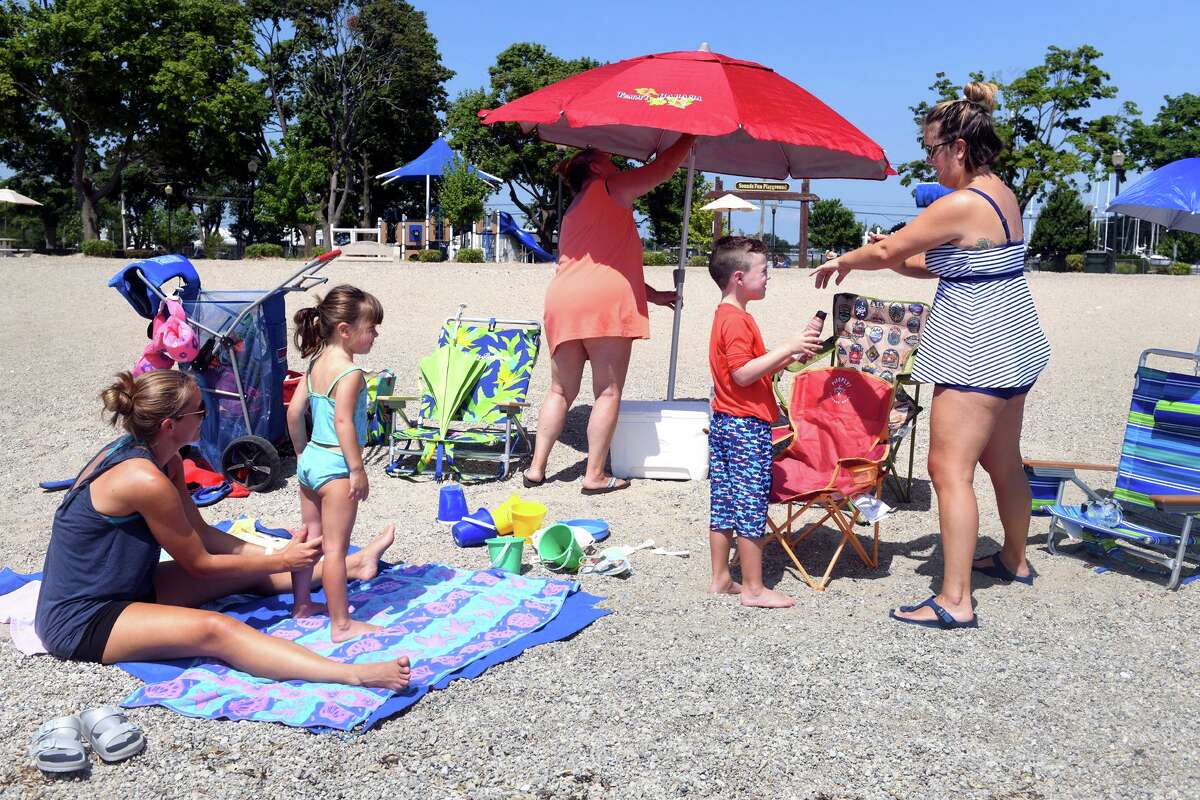 Mary Lou Dolan, center, raises an umbrella while her daughters, Ailene Jayecze, left and Corinne Chiaia, right, help Corinne’s son, Louis, and daughter, Victoria, apply sunscreen during a visit to Calf Pasture Beach, in Norwalk, Conn. July 19, 2022.