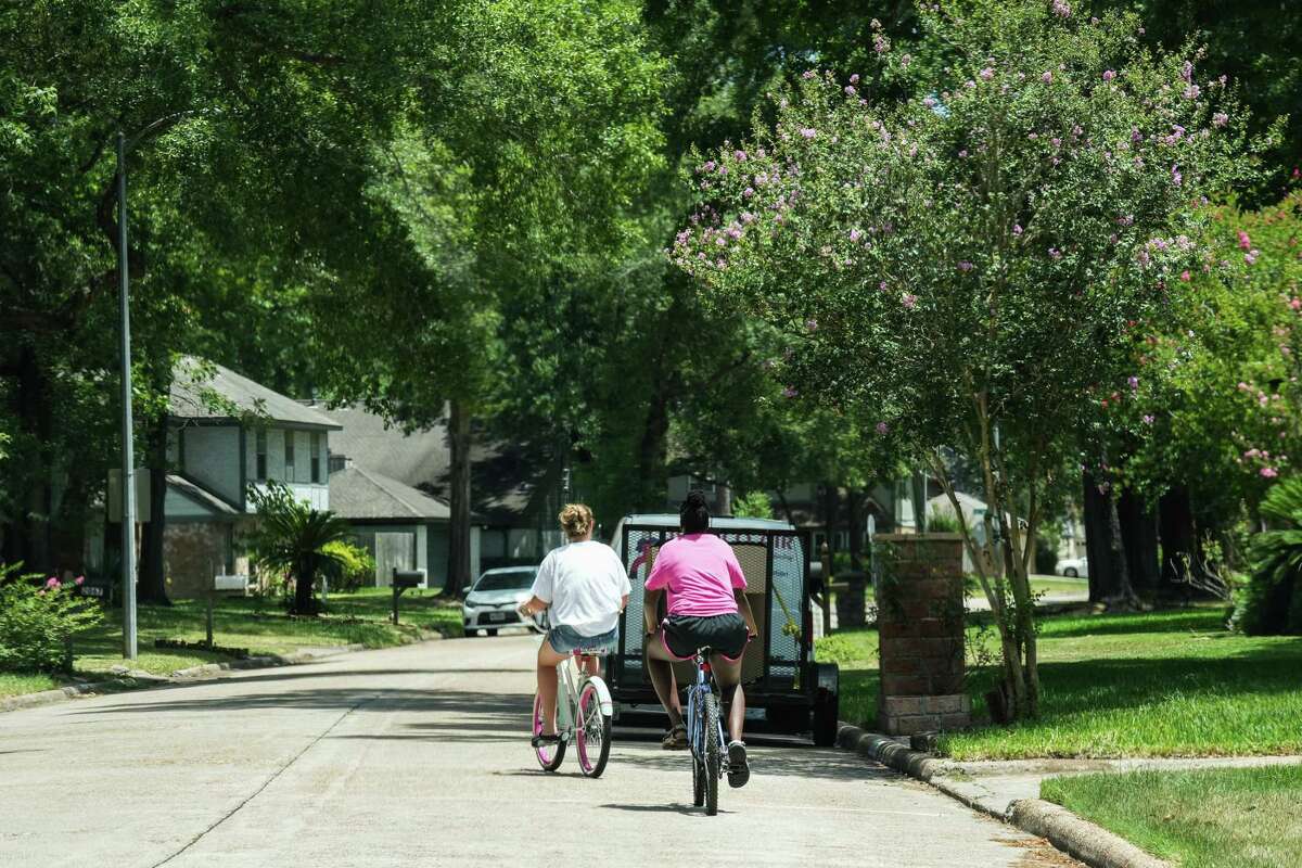Two people ride bikes through the Woodland Hills Village subdivision on Tuesday, July, 19, 2022, in Kingwood, where racist notes were left on the doorstep of a Black family’s home earlier this month.