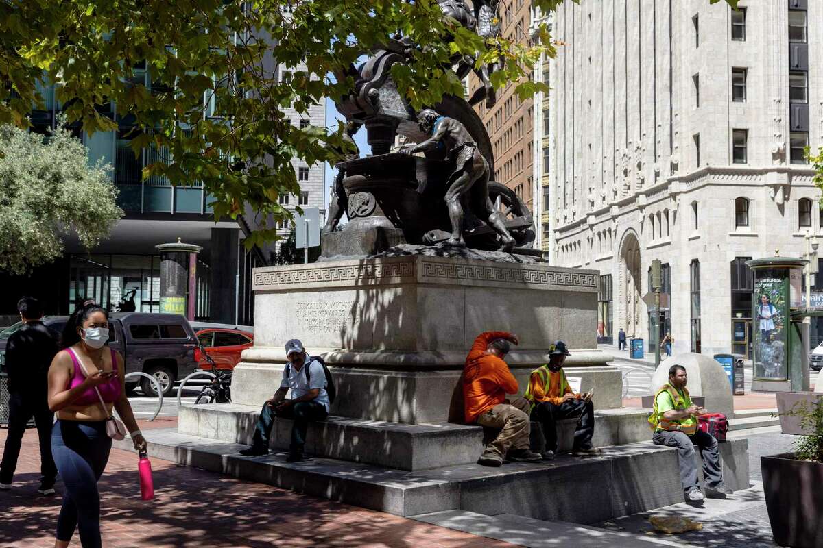 People eat lunch at the foot of a statue inside Mechanics Plaza along Market Street in San Francisco.