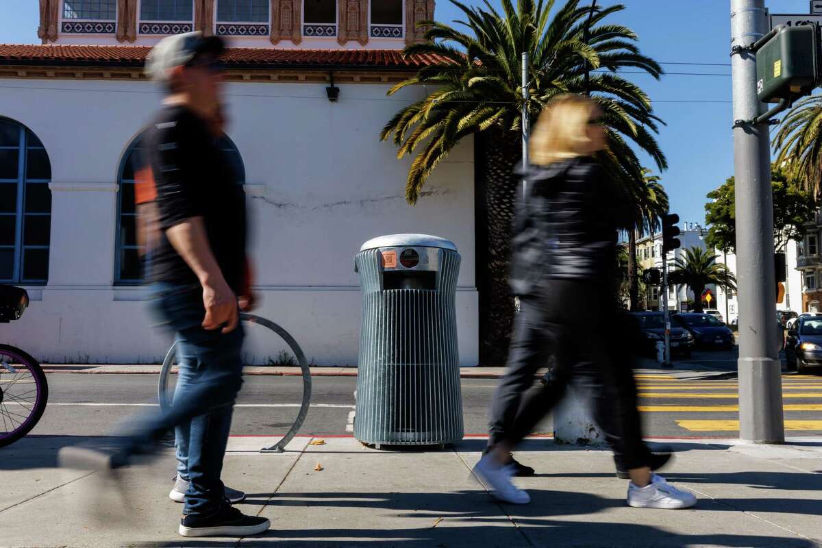 People walk past a prototype of a trash can that San Francisco Public Works is testing on city streets.