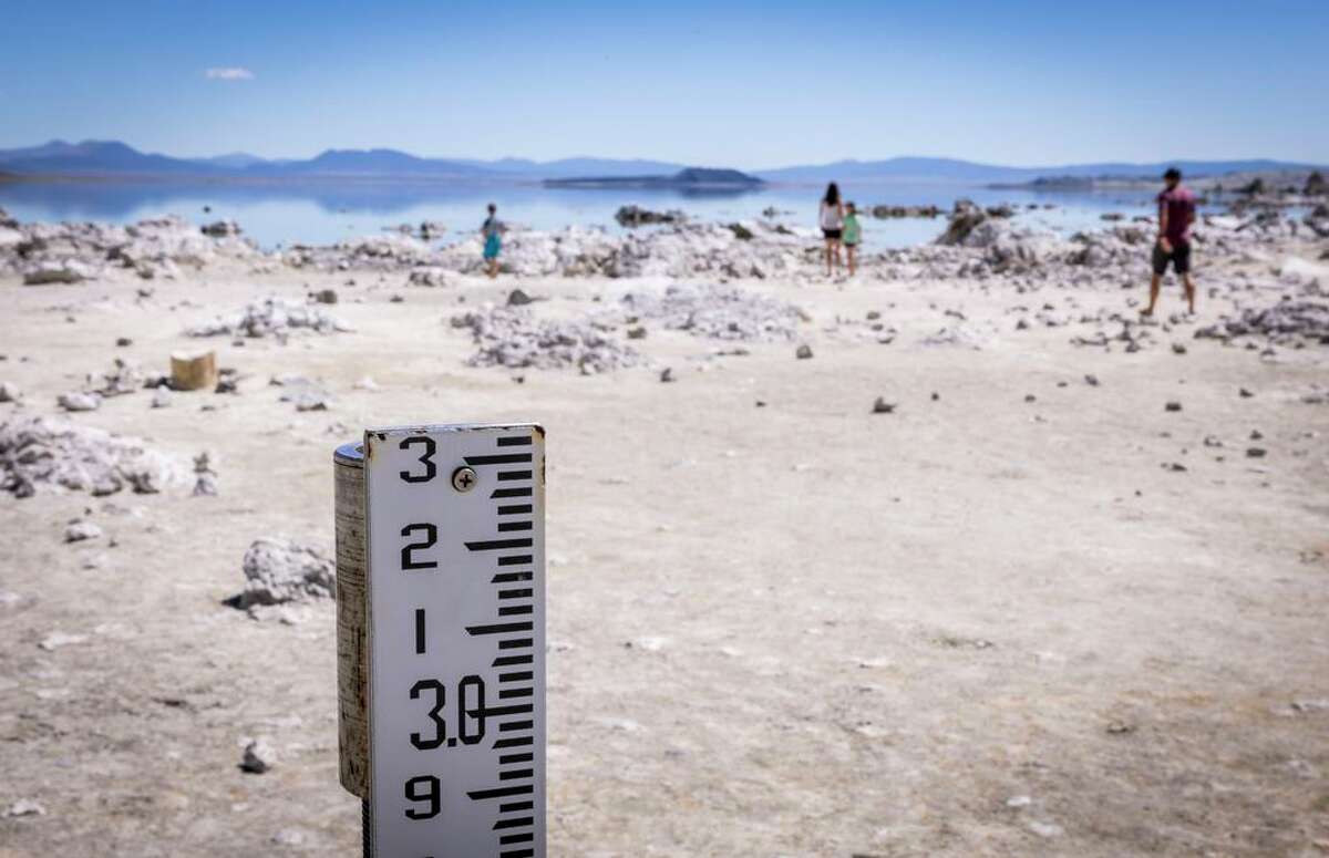 A water measuring gauge sits on dry land and a family checks out the widening shoreline at Mono Lake outside Lee Vining this month. Water levels have been dropping at the lake.