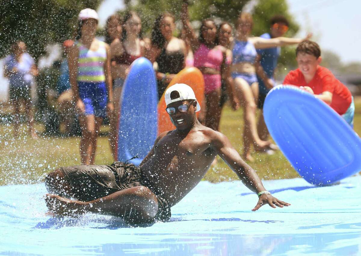 Counselor Myles Henneghan takes a turn on the slip and slide as campers look on at the Norwalk Recreation and Parks Play and Learn summer camp at Calf Pasture Beach in Norwalk, Conn. on Wednesday, July 20, 2022.