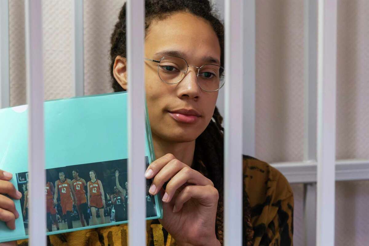 WNBA star and two-time Olympic gold medalist Brittney Griner holds up a photo of players from the recent all star game wearing her number, sitting in a cage at a court room prior to a hearing in the Khimki district court, just outside Moscow, Russia, Friday, July 15, 2022. Griner was arrested in February at the Russian capital's Sheremetyevo Airport when customs officials said they found vape canisters with cannabis oil in her luggage. She has been jailed since then, facing up to 10 years in prison if convicted. (AP Photo/Dmitry Serebryakov)