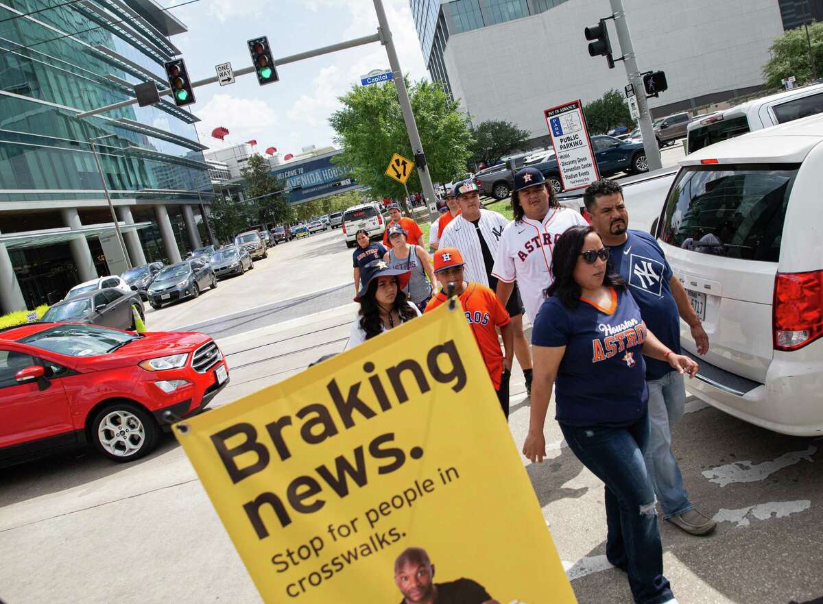 Texas Department of Transportation’s Pedestrian Safety Outreach Team walking as “human billboards” among the Houston Astros fans and crossing Capitol Street on Avenida De Las Americas while the vehicles blocking the crosswalk Thursday, July 21, 2022, near Minute Maid Park in Houston. In the Houston area in 2021, there were 1,466 traffic crashes involving pedestrians, resulting in 204 fatalities and 383 serious injuries, according to TxDOT.